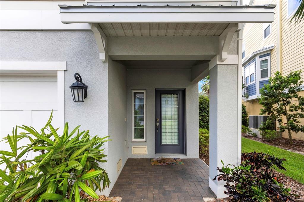 A gray house exterior features a covered entryway with a dark door and brick flooring — 4063 ROCKY SHORES DRIVE, TAMPA, FL