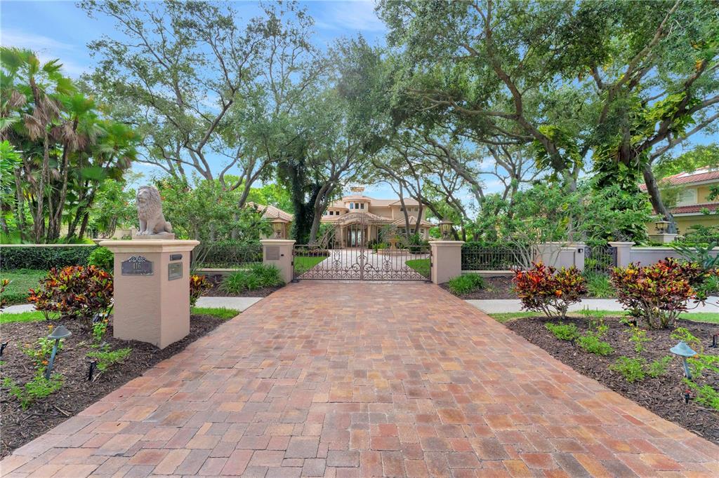 A paved driveway leads to a gated entrance of a house framed by large trees — 416 81ST STREET W, BRADENTON, FL
