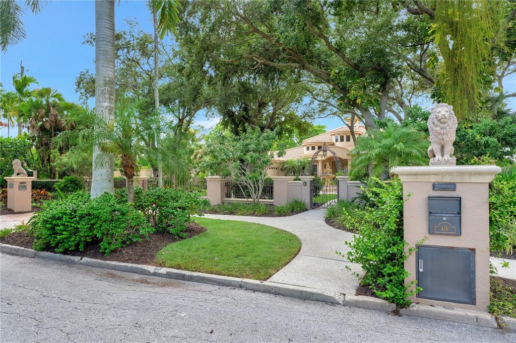 A gated entrance with a lion statue on a pillar leads to a landscaped driveway — 416 81ST STREET W, BRADENTON, FL