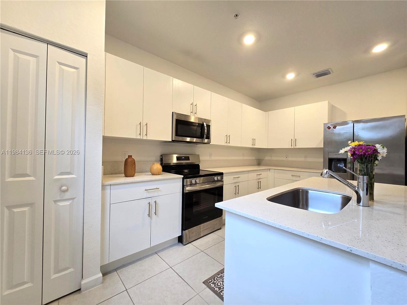 A modern kitchen features white cabinets, stainless steel appliances, and a quartz-topped island — 2761 NW 55th Way, Lauderhill FL 33313, LAUDERHILL, FL
