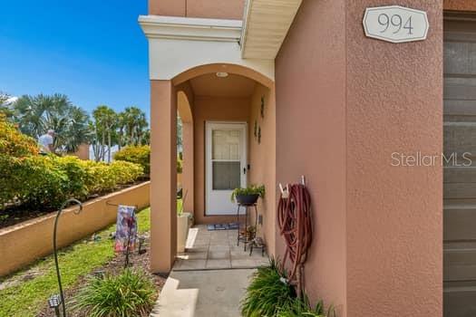 A tan house exterior features a covered entryway, a white front door, and a hose — 994 CELTIC CIRCLE, TARPON SPRINGS, FL