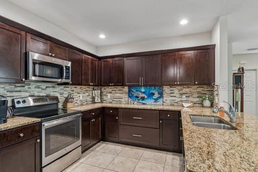 A kitchen features dark wood cabinets, stainless steel appliances, granite countertops, and a tile backsplash — 994 CELTIC CIRCLE, TARPON SPRINGS, FL