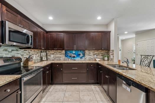 A U-shaped kitchen features dark wood cabinets, granite countertops, stainless steel appliances, and tile flooring — 994 CELTIC CIRCLE, TARPON SPRINGS, FL