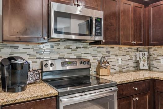 A kitchen features dark wood cabinets, stainless steel appliances, and a mosaic tile backsplash — 994 CELTIC CIRCLE, TARPON SPRINGS, FL