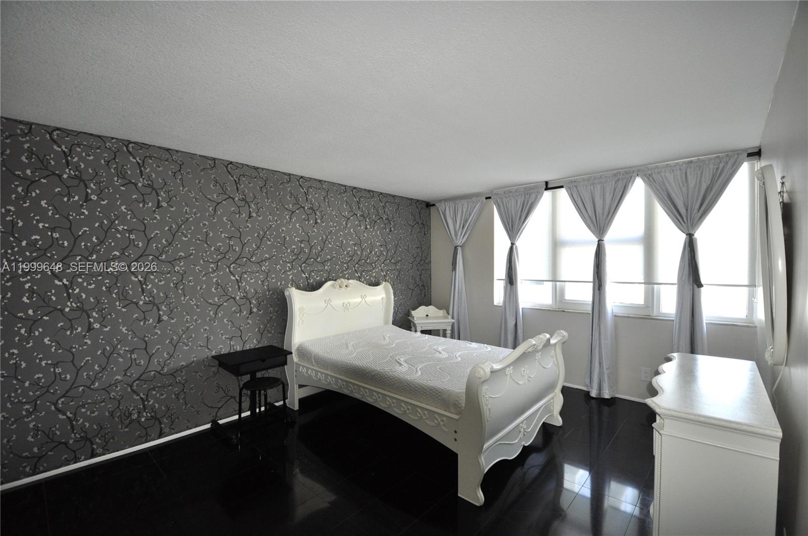 A bedroom features a white bed, dark flooring, and a gray floral accent wall — 2030 S Ocean Dr # 803, Hallandale Beach FL 33009, HALLANDALE BEACH, FL