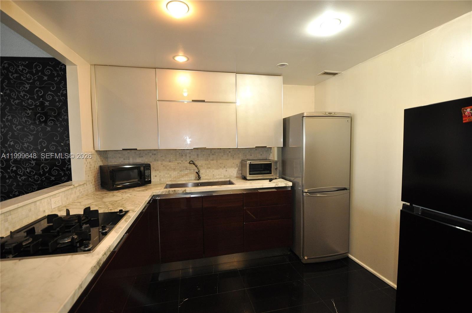 A kitchen features dark wood lower cabinets, white upper cabinets, and black tile flooring — 2030 S Ocean Dr # 803, Hallandale Beach FL 33009, HALLANDALE BEACH, FL