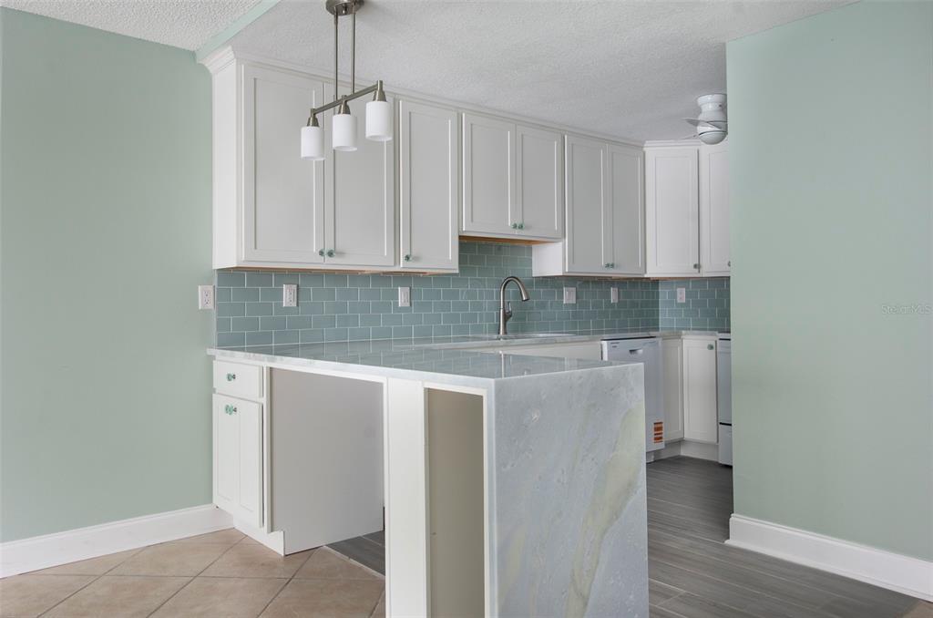 A kitchen features white cabinets, a light blue subway tile backsplash, and a stone peninsula — 450 TREASURE ISLAND CAUSEWAY UNIT 105, TREASURE ISLAND, FL