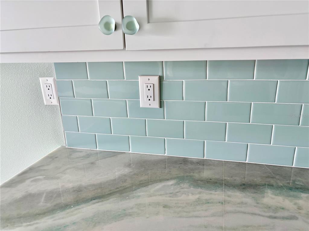 A kitchen backsplash features light blue subway tiles, white cabinets, and a marbled countertop — 450 TREASURE ISLAND CAUSEWAY UNIT 105, TREASURE ISLAND, FL