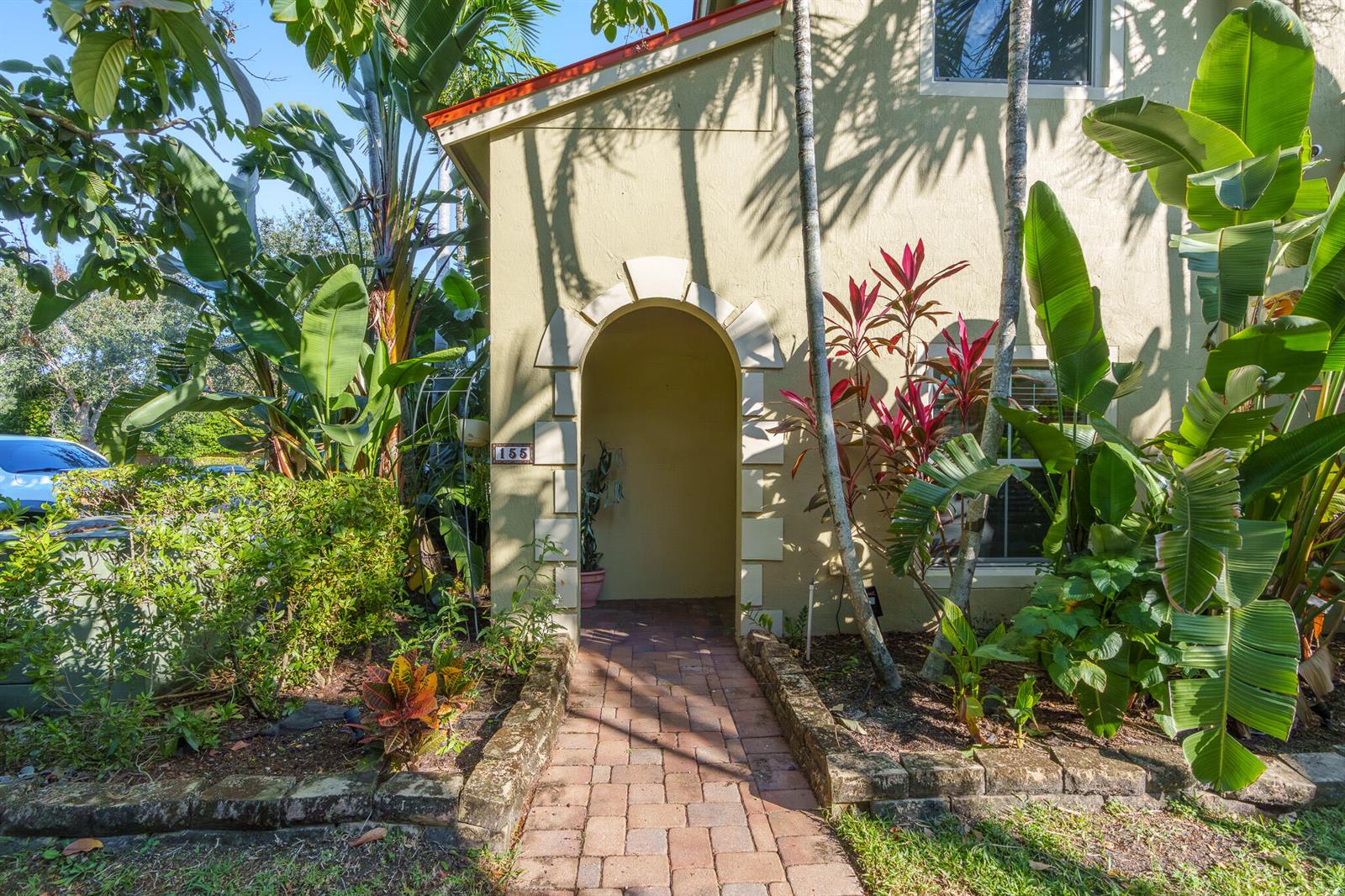 A brick walkway leads to the arched entryway of a tan house with lush landscaping — 155 Monterey Bay Drive, Boynton Beach FL 33426, BOYNTON BEACH, FL