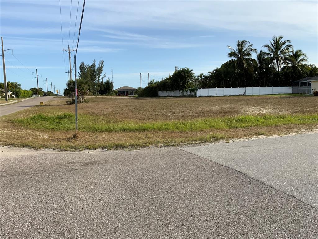 A vacant, grassy residential lot sits at a street corner with palm trees in the background — 2000 SW 28TH TERRACE, CAPE CORAL, FL
