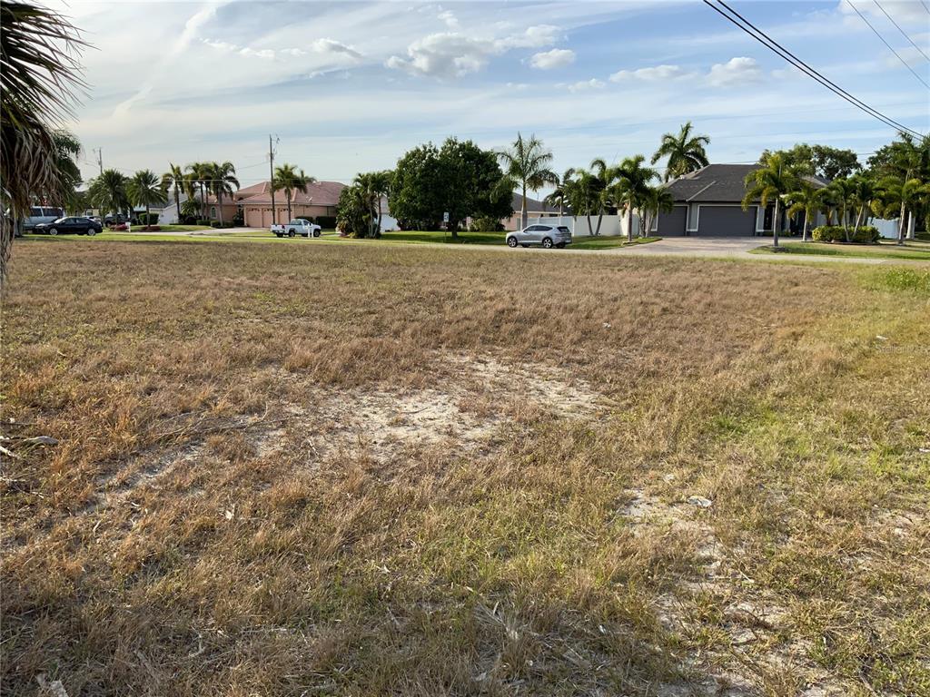 A vacant, grassy residential lot with palm trees and houses in the background — 2000 SW 28TH TERRACE, CAPE CORAL, FL