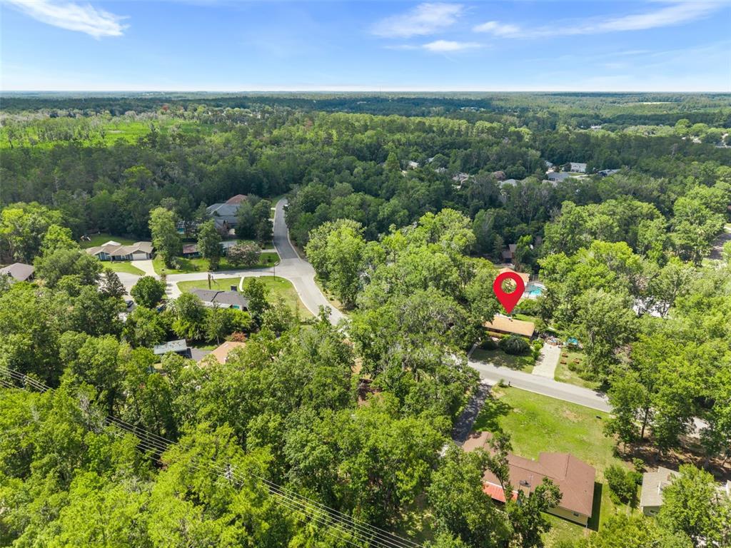 An aerial view shows a house with a red location pin in a wooded neighborhood — 10503 NW 25TH PLACE, GAINESVILLE, FL