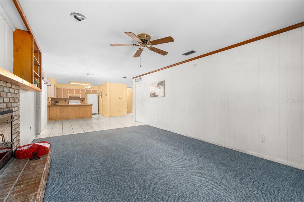 A living room with blue carpet and white wood paneling leads to an open kitchen — 10503 NW 25TH PLACE, GAINESVILLE, FL