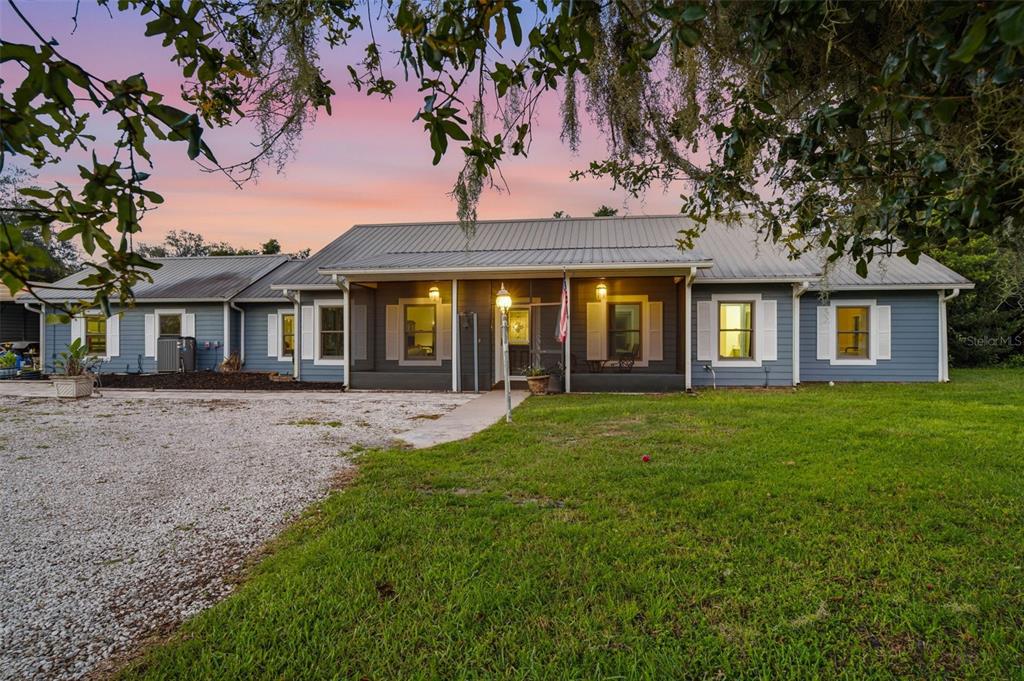 A single-story blue house with a metal roof and a gravel driveway at sunset — 1690 TALLAPOOSA DRIVE, GENEVA, FL