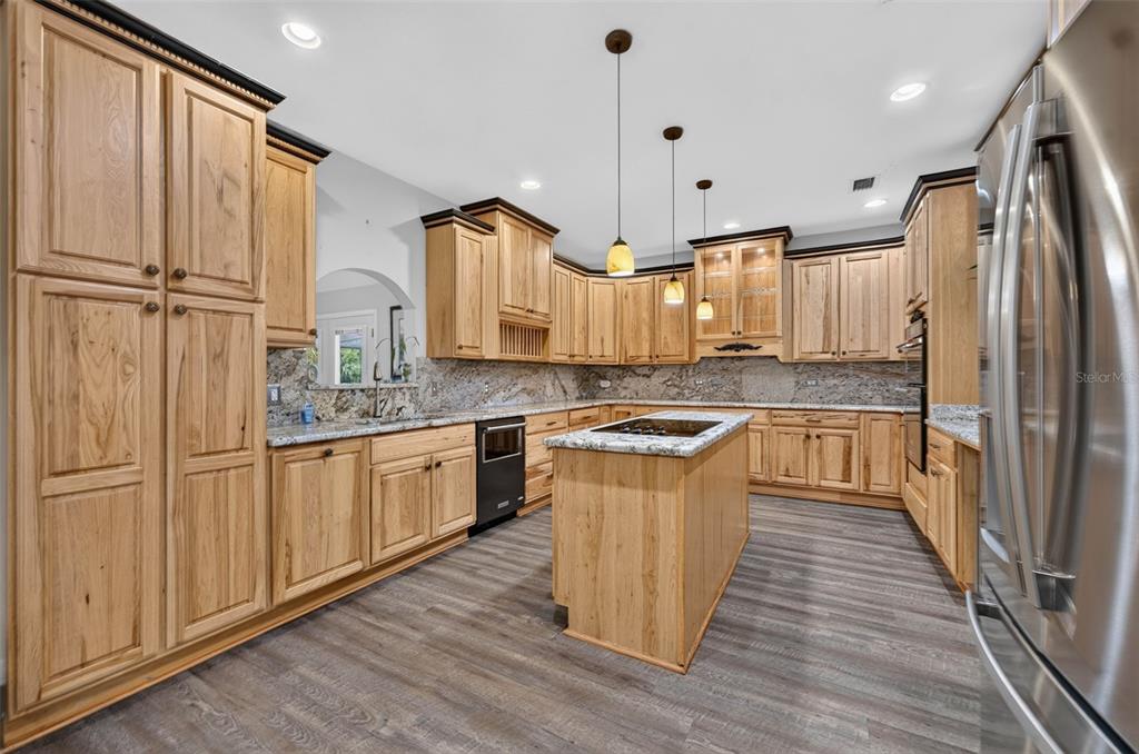 A kitchen with light wood cabinets, granite countertops, a center island, and gray wood-look flooring — 1690 TALLAPOOSA DRIVE, GENEVA, FL