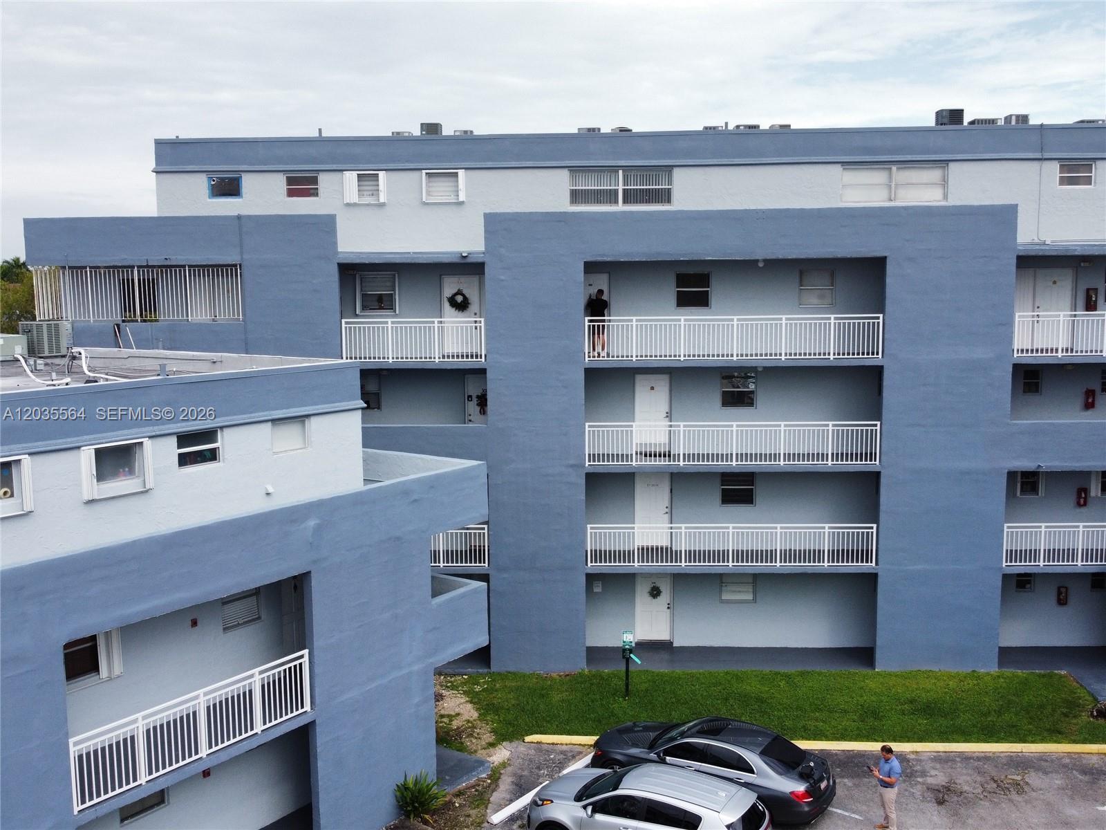 An exterior view of a multi-story blue apartment building with white railings and a parking lot — 9351 Fontainebleau Blvd # B403, Miami FL 33172, MIAMI, FL