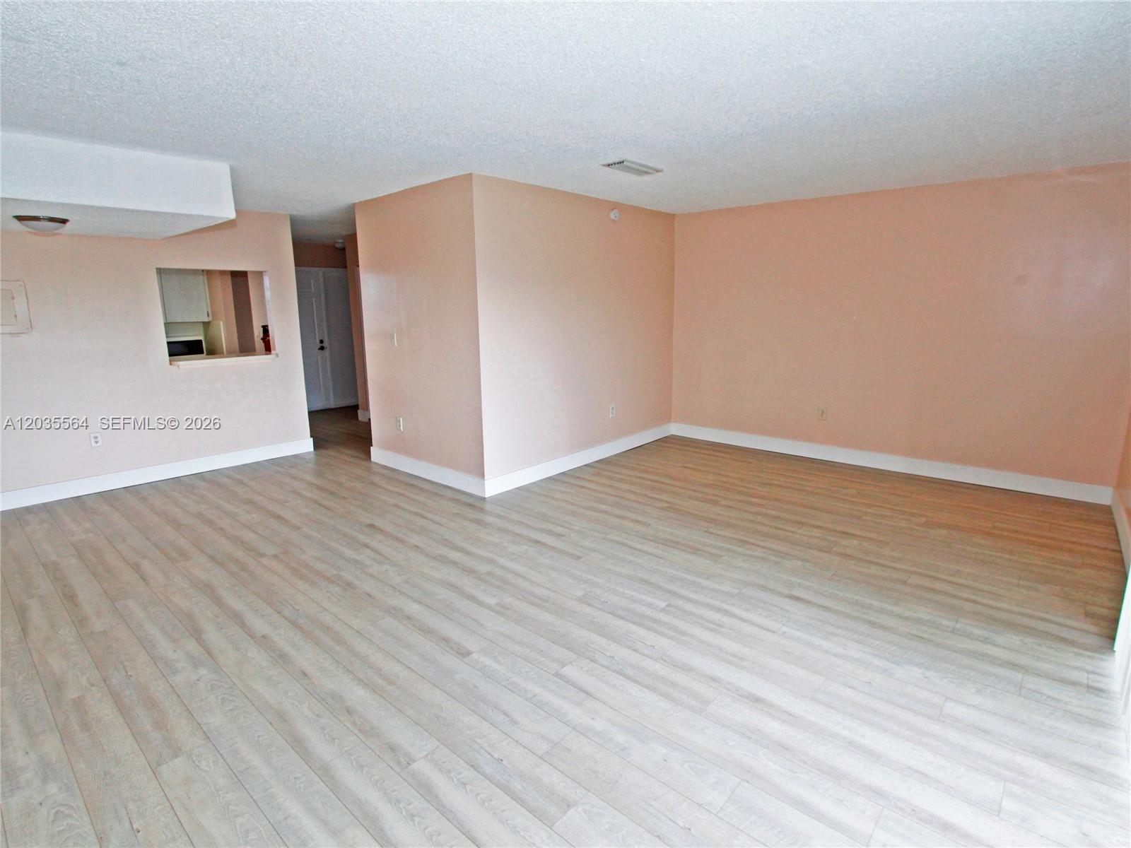 An empty living room features light wood-look flooring and peach-colored walls — 9351 Fontainebleau Blvd # B403, Miami FL 33172, MIAMI, FL