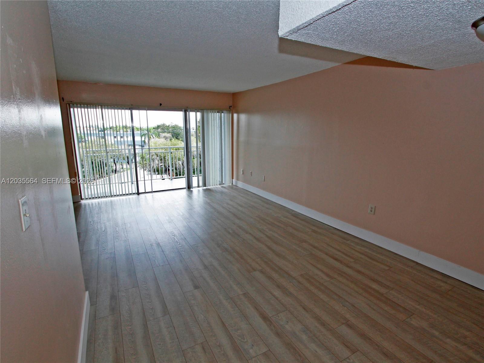 An empty room features light wood-look flooring, peach-colored walls, and a sliding glass door — 9351 Fontainebleau Blvd # B403, Miami FL 33172, MIAMI, FL