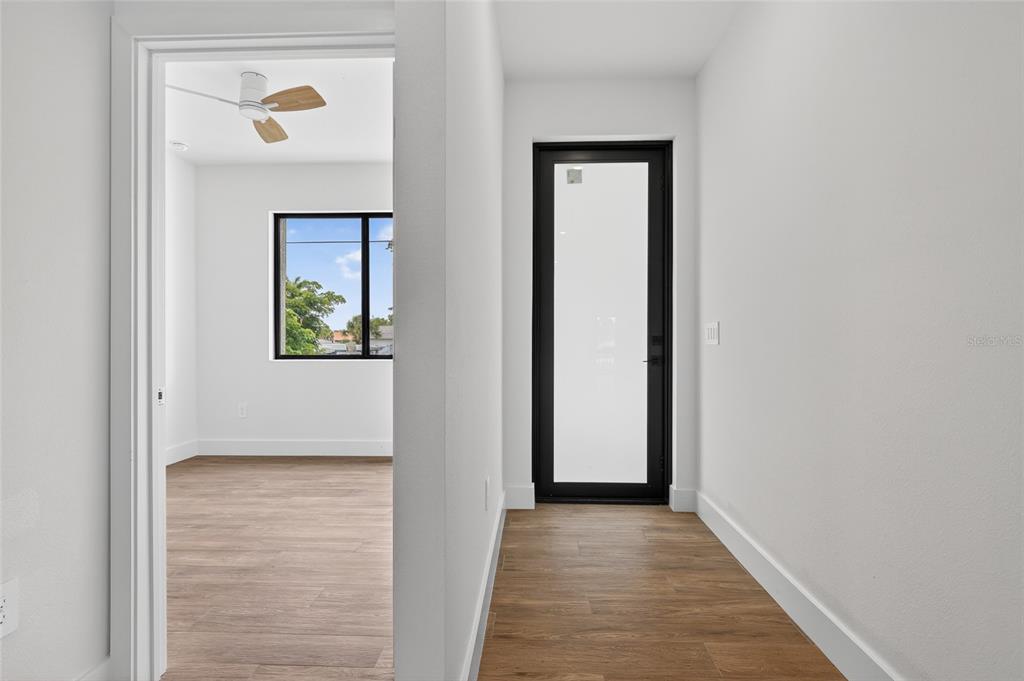A hallway with wood-look flooring leads to a glass-paneled door and an adjacent bedroom — 1018 S MARLIN DRIVE, PUNTA GORDA, FL