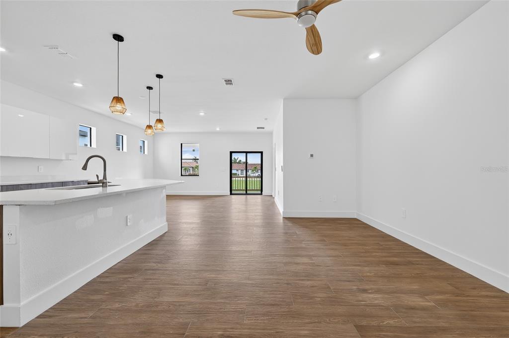 A bright, open-concept kitchen and living area features white cabinetry, pendant lighting, and wood-look flooring — 1018 S MARLIN DRIVE, PUNTA GORDA, FL