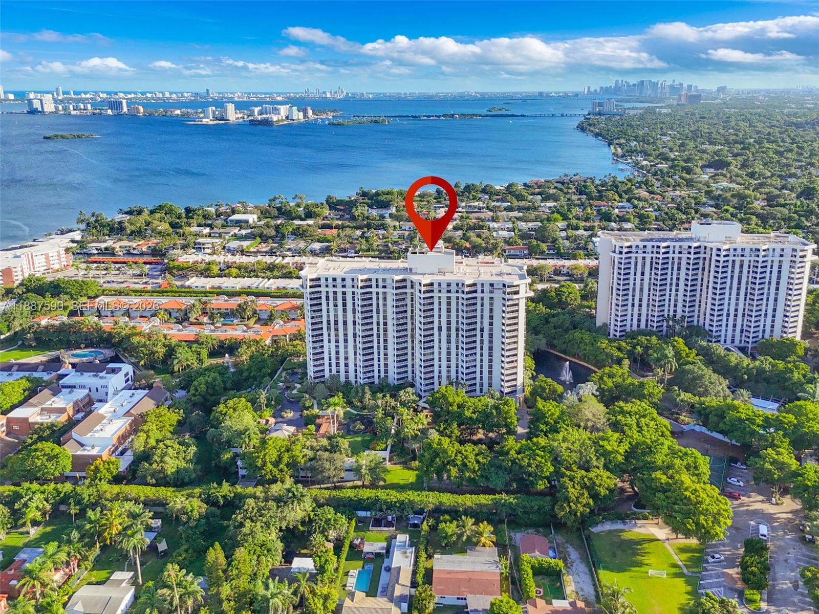 An aerial view shows a tall residential building surrounded by trees near a large bay — 1000 Quayside Ter # 505, Miami FL 33138, MIAMI, FL