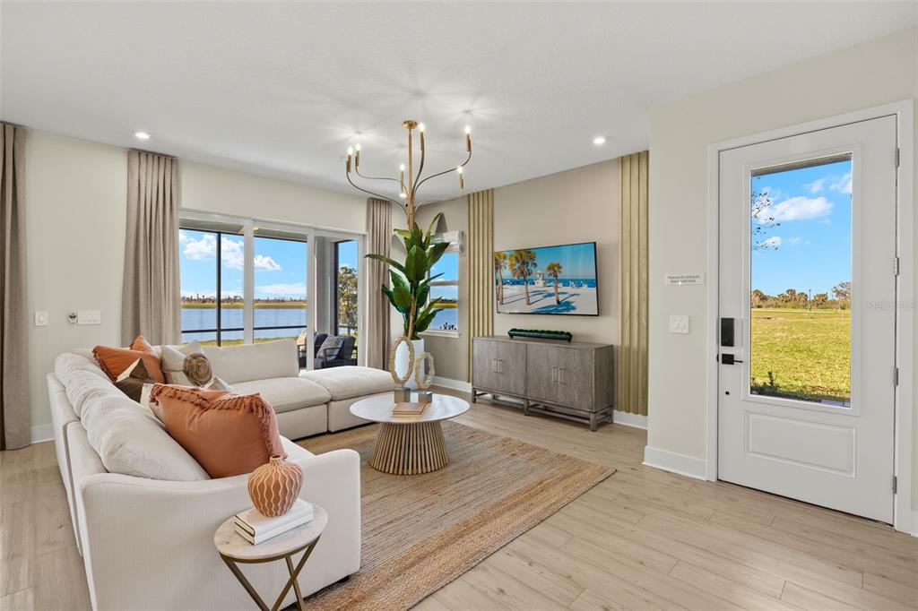 A bright living room features a sectional sofa, a modern chandelier, and a view of water — 12829 JADE EMPRESS LOOP UNIT 101, VENICE, FL