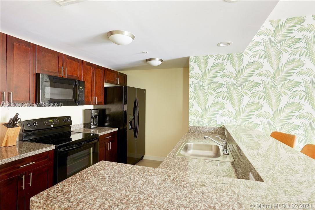 A living room features palm-leaf wallpaper, a yellow sofa, and an adjacent open kitchen — 568 NE 66th St # 501, Miami FL 33138, MIAMI, FL