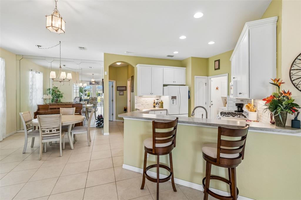 A kitchen with white cabinets and a breakfast bar overlooks a dining area with mirrors — 2011 SIFIELD GREENS WAY UNIT 71, SUN CITY CENTER, FL