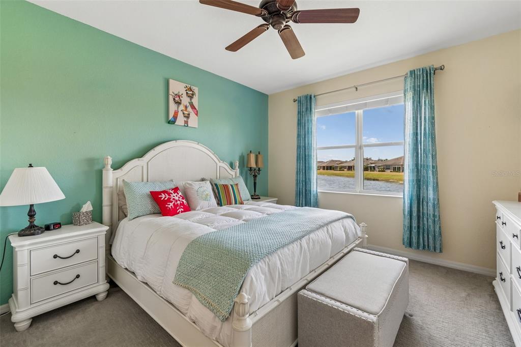 A bedroom features a white bed, teal accent wall, and a window overlooking a lake — 2011 SIFIELD GREENS WAY UNIT 71, SUN CITY CENTER, FL