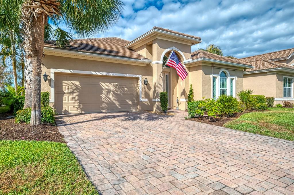 A single-story beige house with a paved driveway, a two-car garage, and an American flag — 13344 CREEKSIDE LANE, PORT CHARLOTTE, FL
