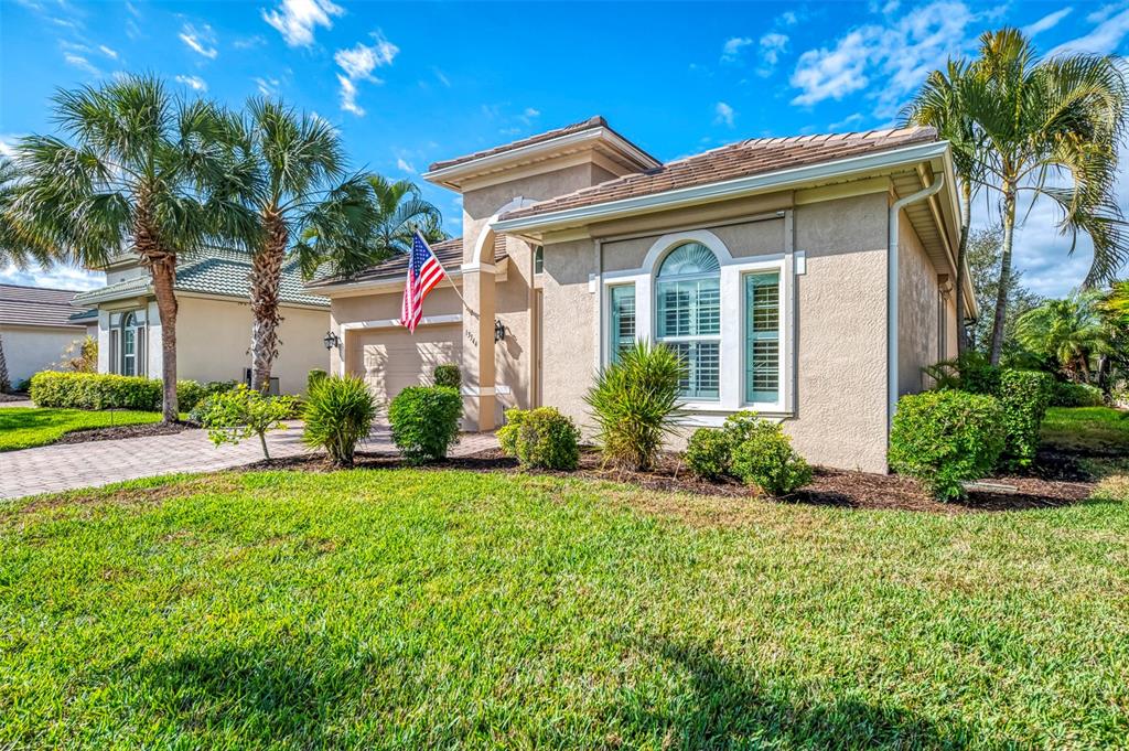 A single-story tan stucco house with a tiled roof, palm trees, and a front lawn — 13344 CREEKSIDE LANE, PORT CHARLOTTE, FL