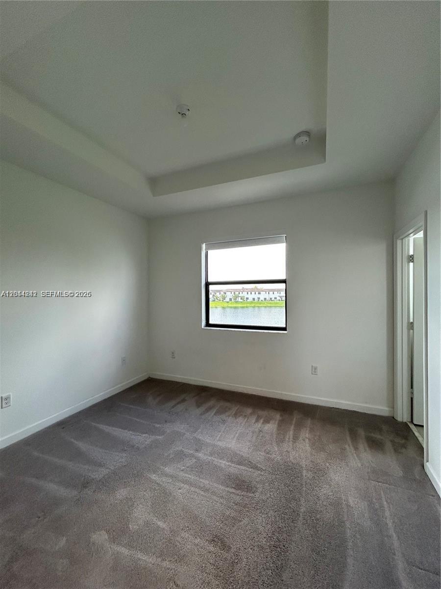 An empty bedroom features gray carpeting, a tray ceiling, and a window overlooking a lake — 22913 SW 99th Ave, Cutler Bay FL 33190, CUTLER BAY, FL