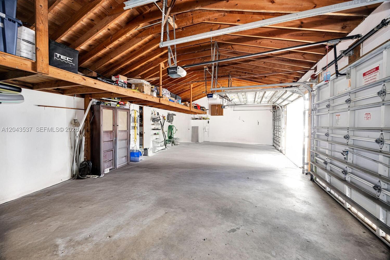 A spacious garage with a concrete floor, exposed wooden rafters, and overhead storage shelving — 940 Sevilla Ave # 206, Coral Gables FL 33134, CORAL GABLES, FL