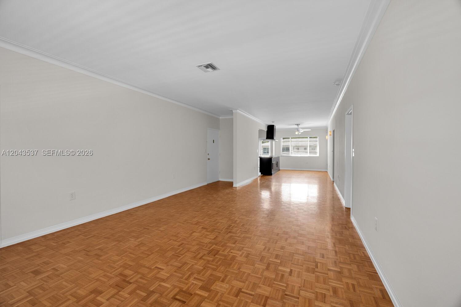 An empty room with parquet wood flooring leads to a kitchen with dark cabinets — 940 Sevilla Ave # 206, Coral Gables FL 33134, CORAL GABLES, FL