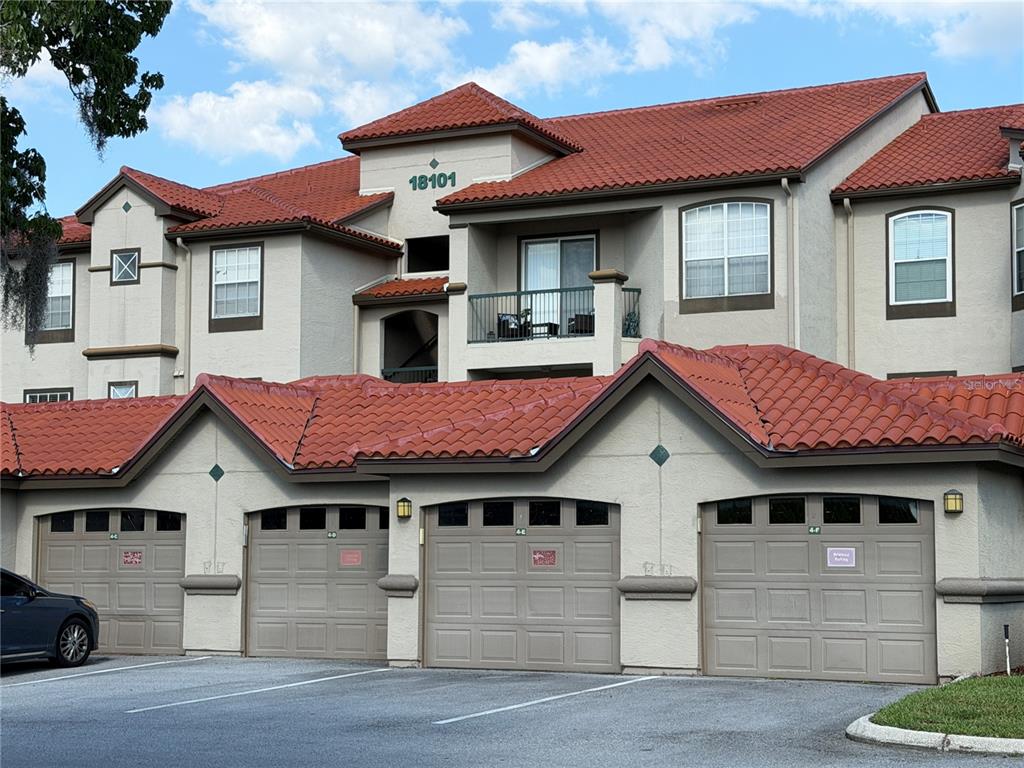 A multi-story apartment building with a red tile roof and a row of garage doors — 18101 PEREGRINES PERCH PLACE UNIT 4201, LUTZ, FL
