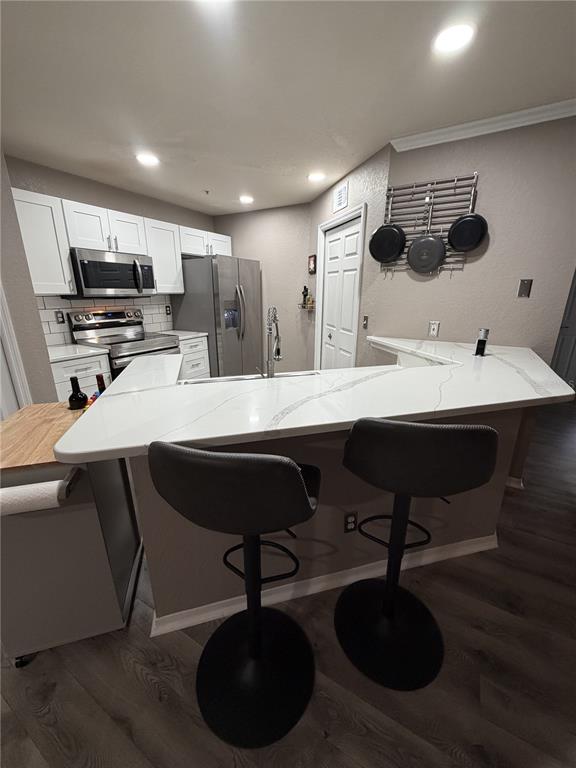 A kitchen features white cabinets, stainless steel appliances, a quartz countertop island, and two stools — 18101 PEREGRINES PERCH PLACE UNIT 4201, LUTZ, FL