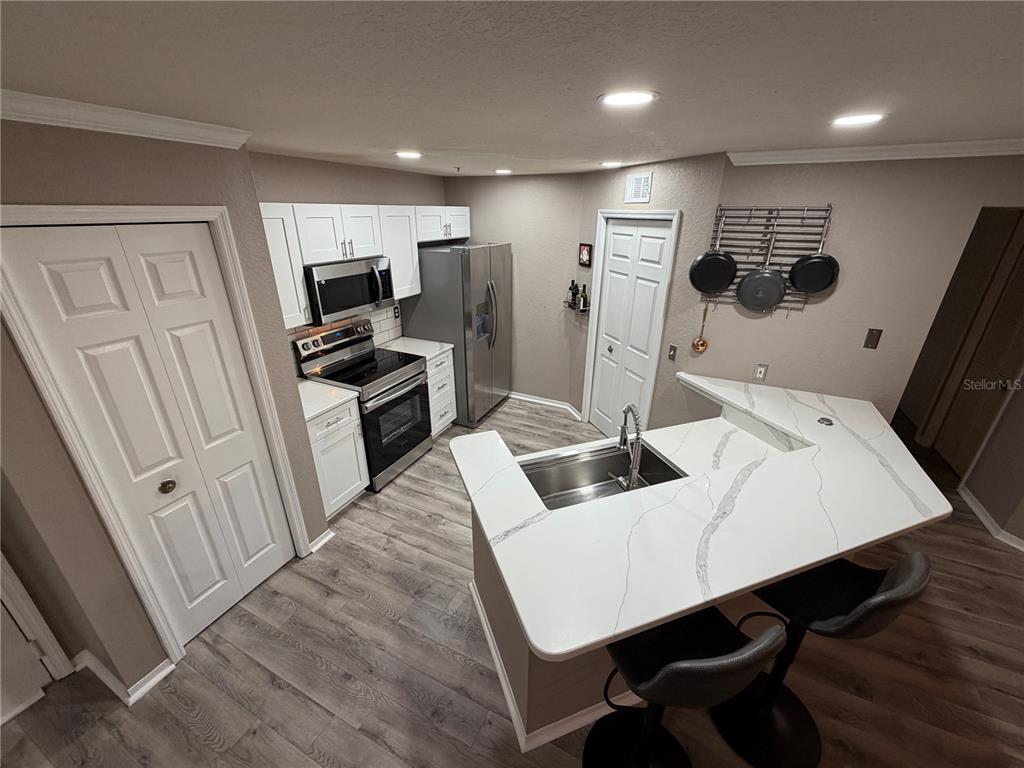 A kitchen features white cabinets, stainless steel appliances, and a white quartz breakfast bar — 18101 PEREGRINES PERCH PLACE UNIT 4201, LUTZ, FL