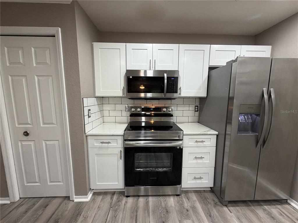 A kitchen features white cabinets, stainless steel appliances, a subway tile backsplash, and wood flooring — 18101 PEREGRINES PERCH PLACE UNIT 4201, LUTZ, FL
