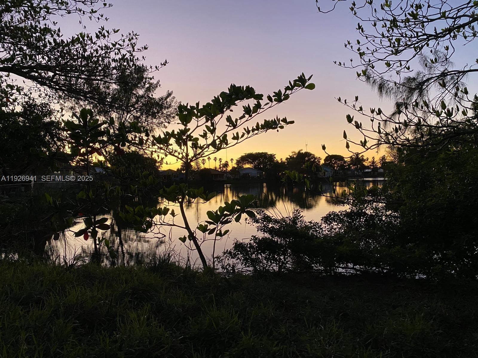 A sunset view over a calm lake framed by silhouetted trees and foliage — 0 SW 10th Ave, Hallandale Beach FL 33009, HALLANDALE BEACH, FL