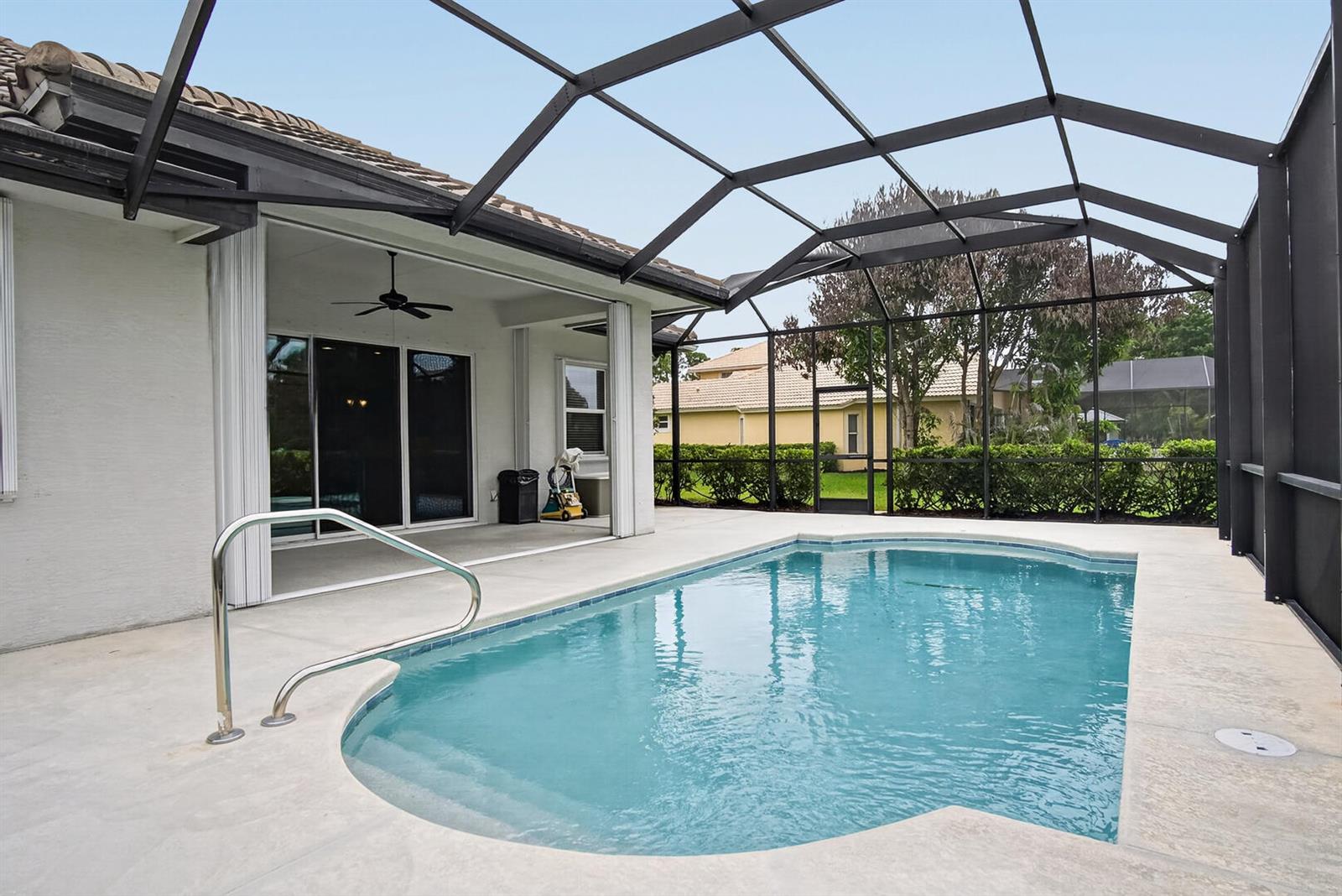 A swimming pool with a metal handrail sits inside a screened-in patio area — 9531 Shadow Lane, Fort Pierce FL 34951, FORT PIERCE, FL
