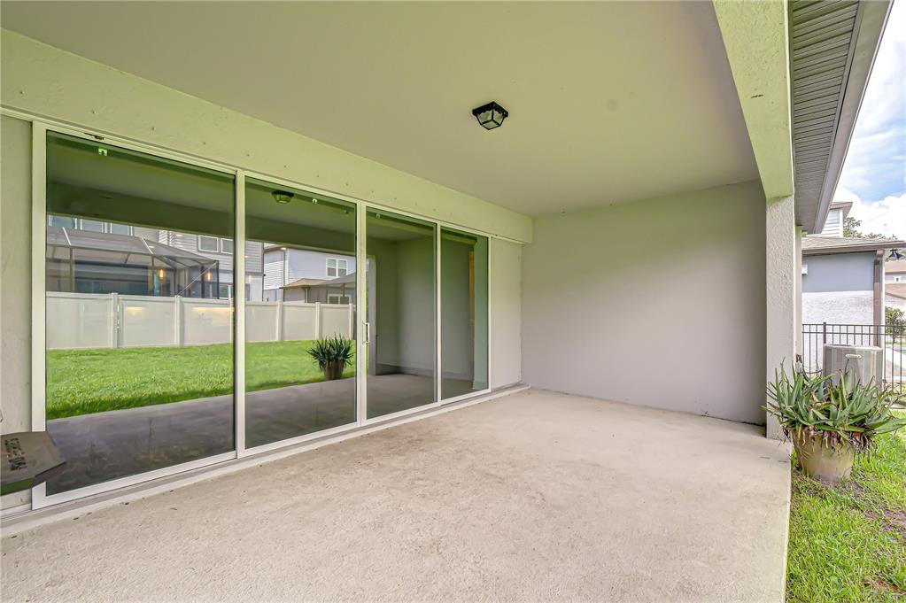 A covered concrete patio features large sliding glass doors and a view of a fenced yard — 13857 SHARP HAWK DRIVE, RIVERVIEW, FL