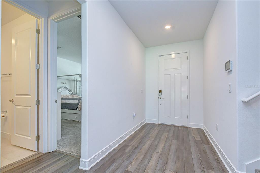 A hallway with wood-look flooring leads to a white door and an adjacent bedroom entrance — 13857 SHARP HAWK DRIVE, RIVERVIEW, FL