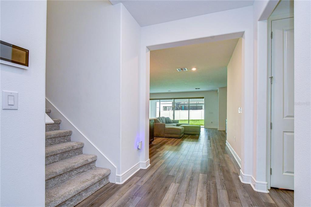 An entryway with carpeted stairs leads to an open-concept living area with wood-look flooring — 13857 SHARP HAWK DRIVE, RIVERVIEW, FL