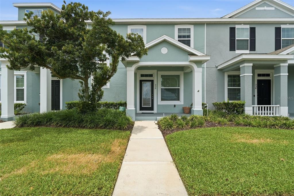 A light blue two-story townhouse with a covered front porch and a paved walkway — 556 JUNIPER SPRINGS DRIVE, GROVELAND, FL