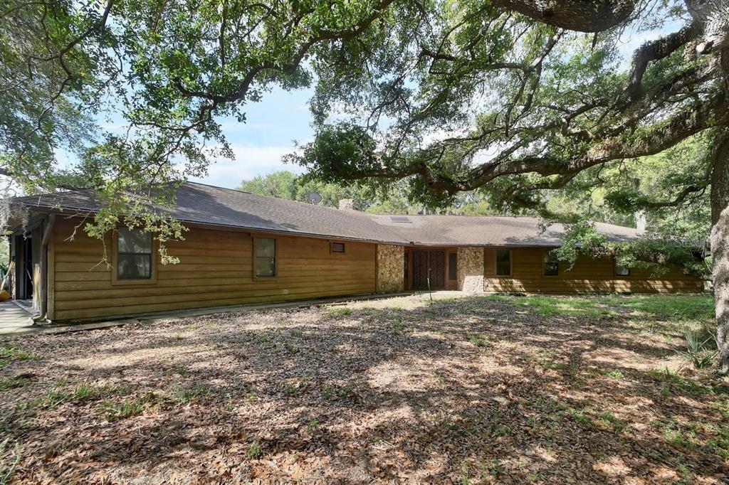 A single-story house with wood siding and stone accents sits under large oak trees — 175 BAYWOOD DRIVE, OAK HILL, FL