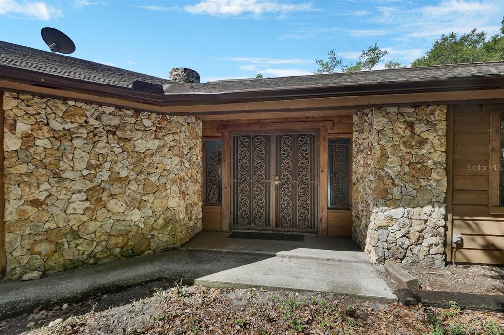 A stone-clad house exterior features a double front door with decorative metal security screens — 175 BAYWOOD DRIVE, OAK HILL, FL