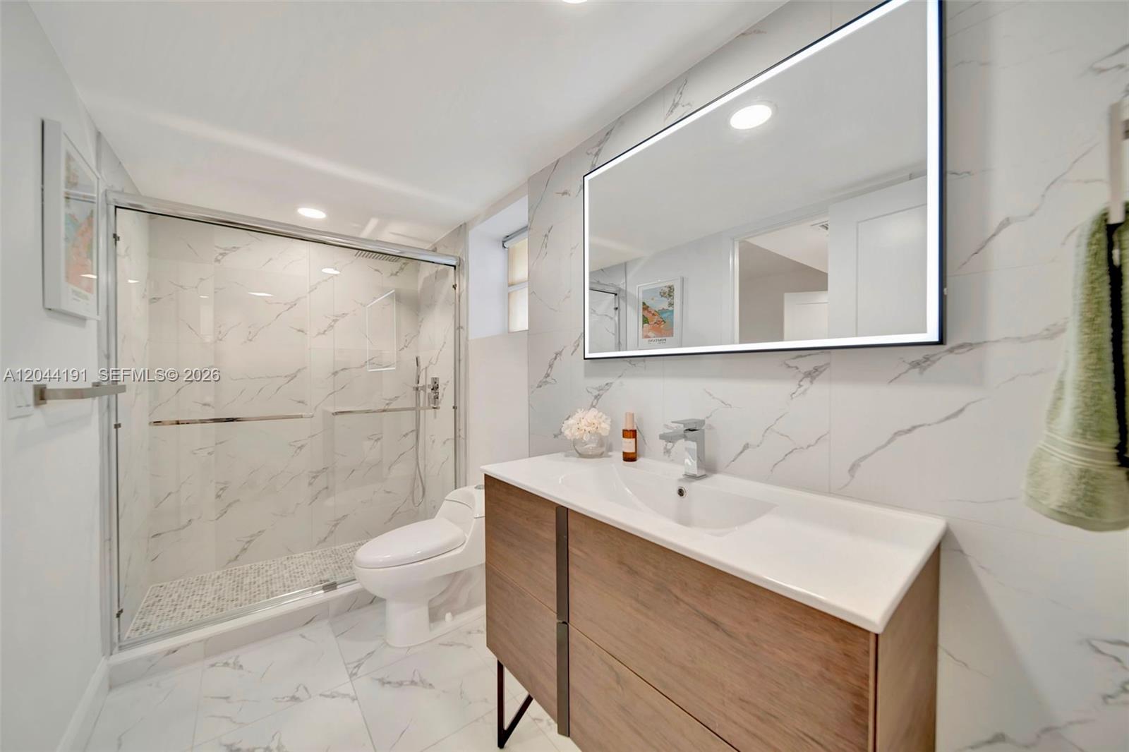 A modern bathroom features a glass-enclosed shower, a wood vanity, and white marble-patterned tile — 3100 Holiday Springs Blvd # 111, Margate FL 33063, MARGATE, FL