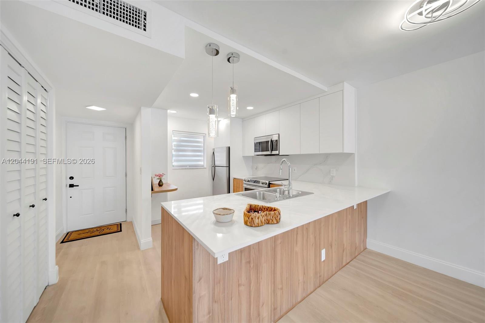 A modern kitchen features a white quartz island, light wood cabinetry, and stainless steel appliances — 3100 Holiday Springs Blvd # 111, Margate FL 33063, MARGATE, FL
