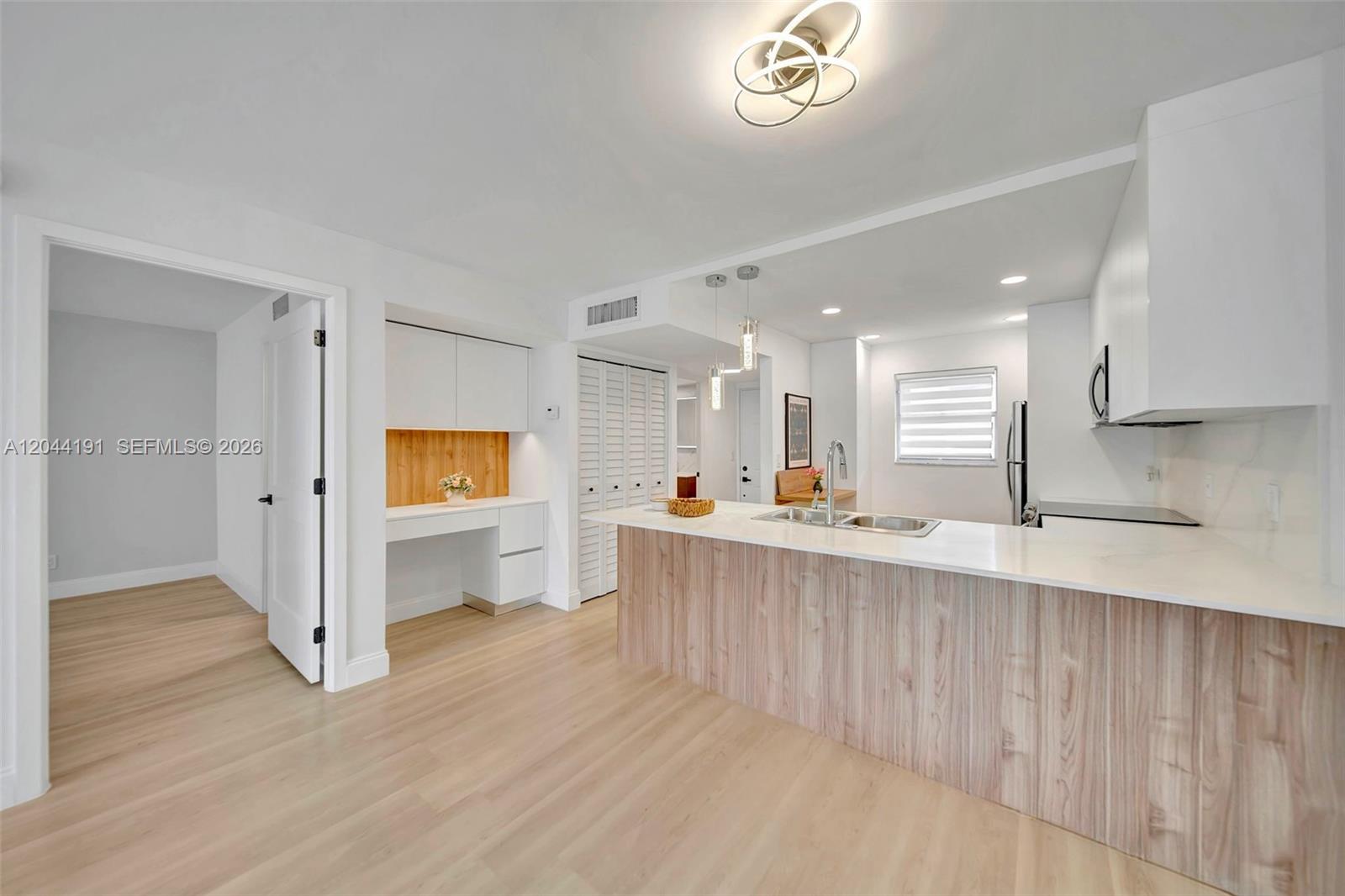 A modern kitchen features a wood-paneled island, white cabinetry, and an adjacent built-in desk area — 3100 Holiday Springs Blvd # 111, Margate FL 33063, MARGATE, FL