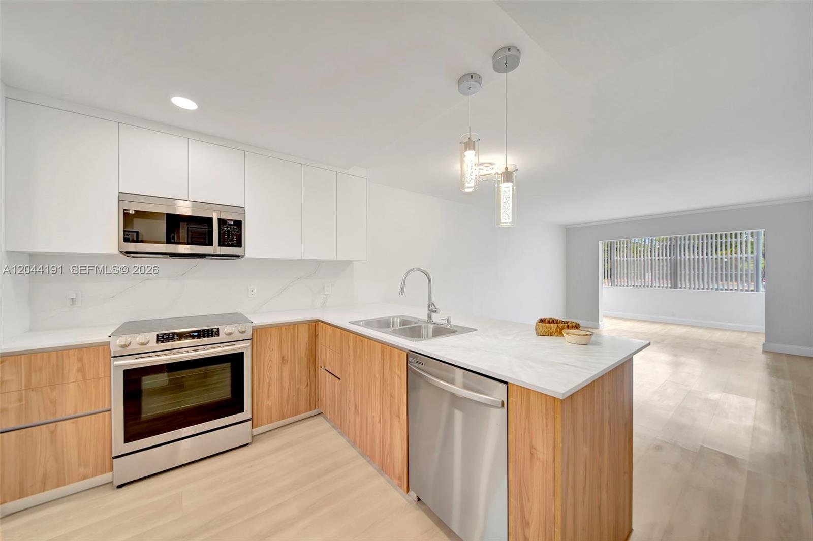 A modern kitchen features white upper cabinets, wood lower cabinets, and stainless steel appliances — 3100 Holiday Springs Blvd # 111, Margate FL 33063, MARGATE, FL